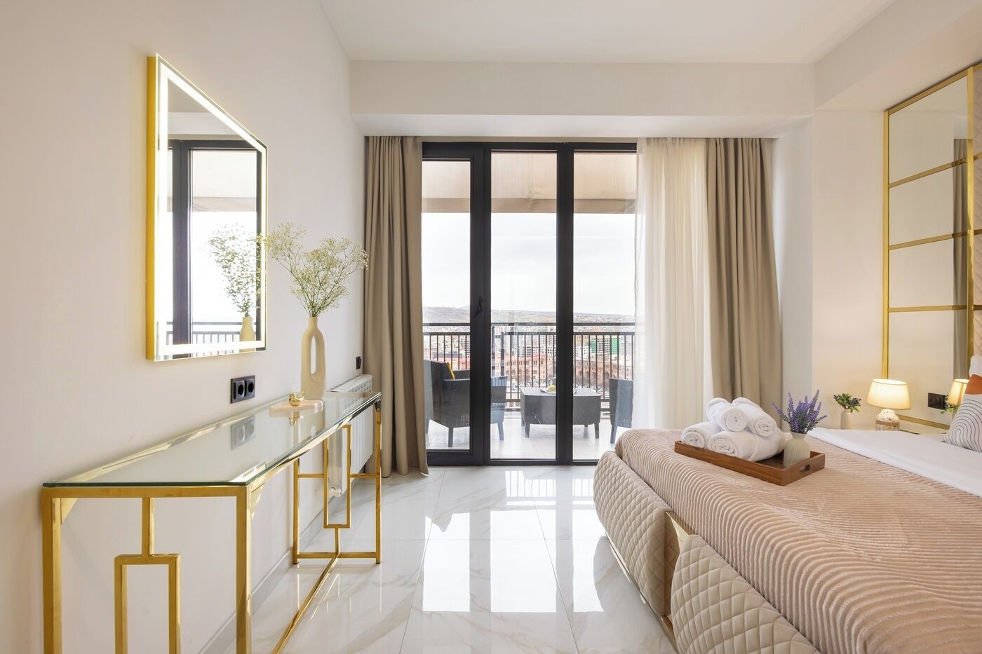 A hotel room with a bed, a bedside table, a mirror, a glass partition, and a view of the outside.