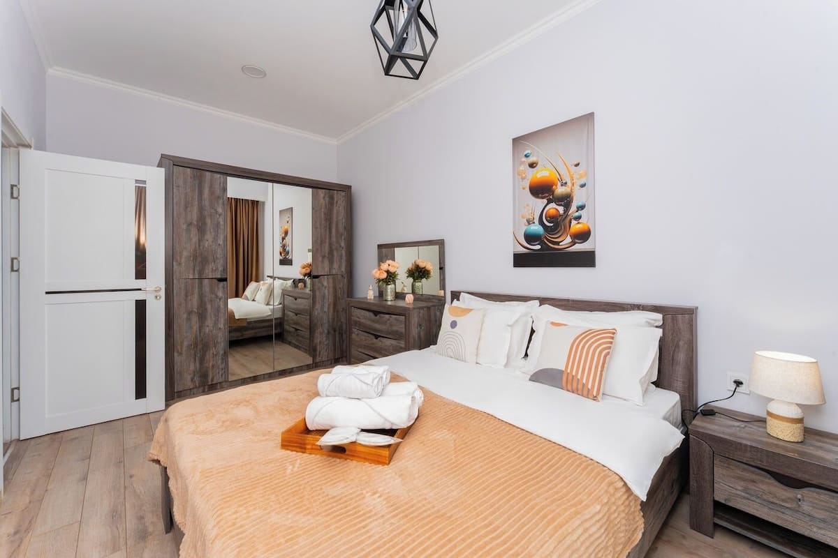 A modern hotel room with a large bed, a wardrobe, a mirror, and a painting on the wall.