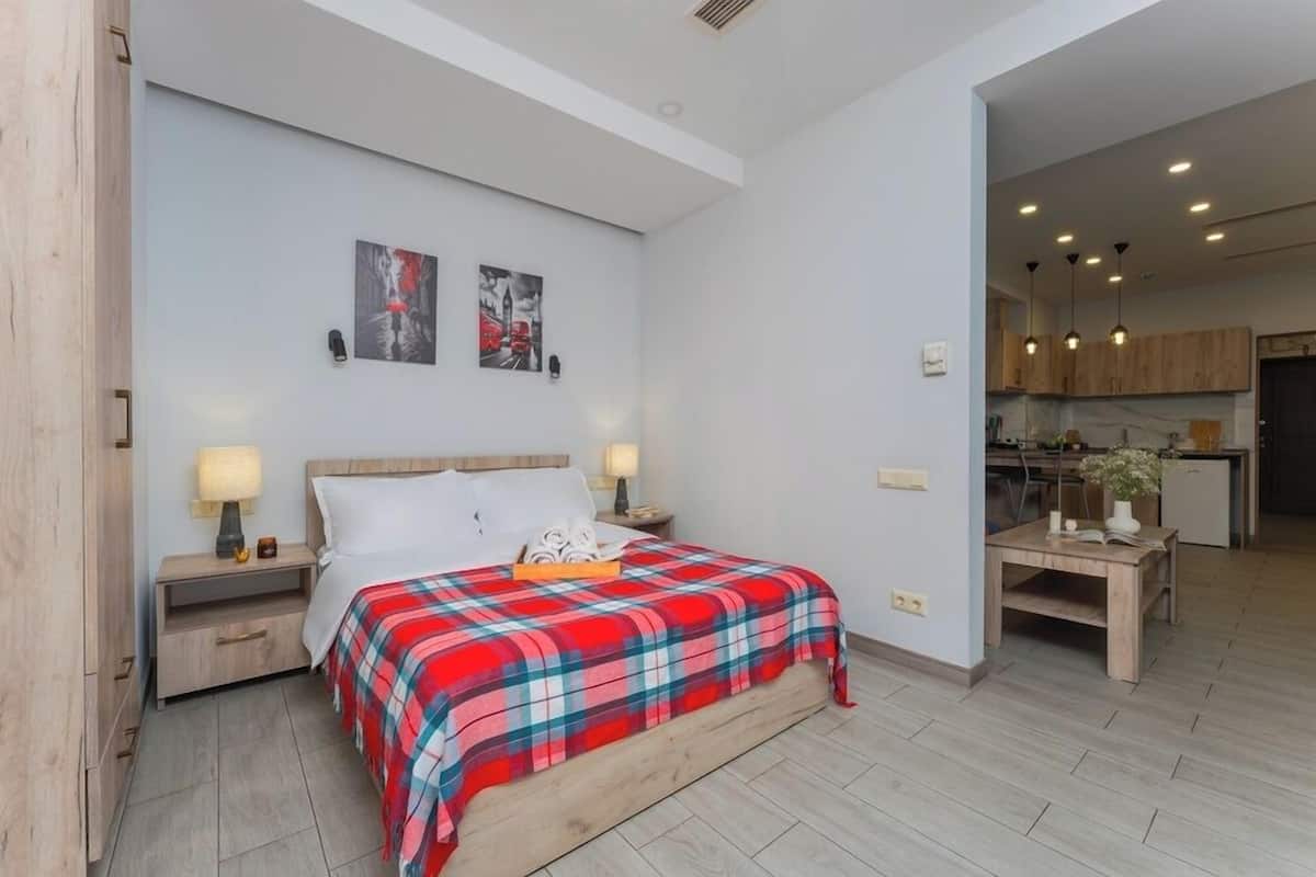 A bedroom with a bed, nightstands, and a view into the kitchen.