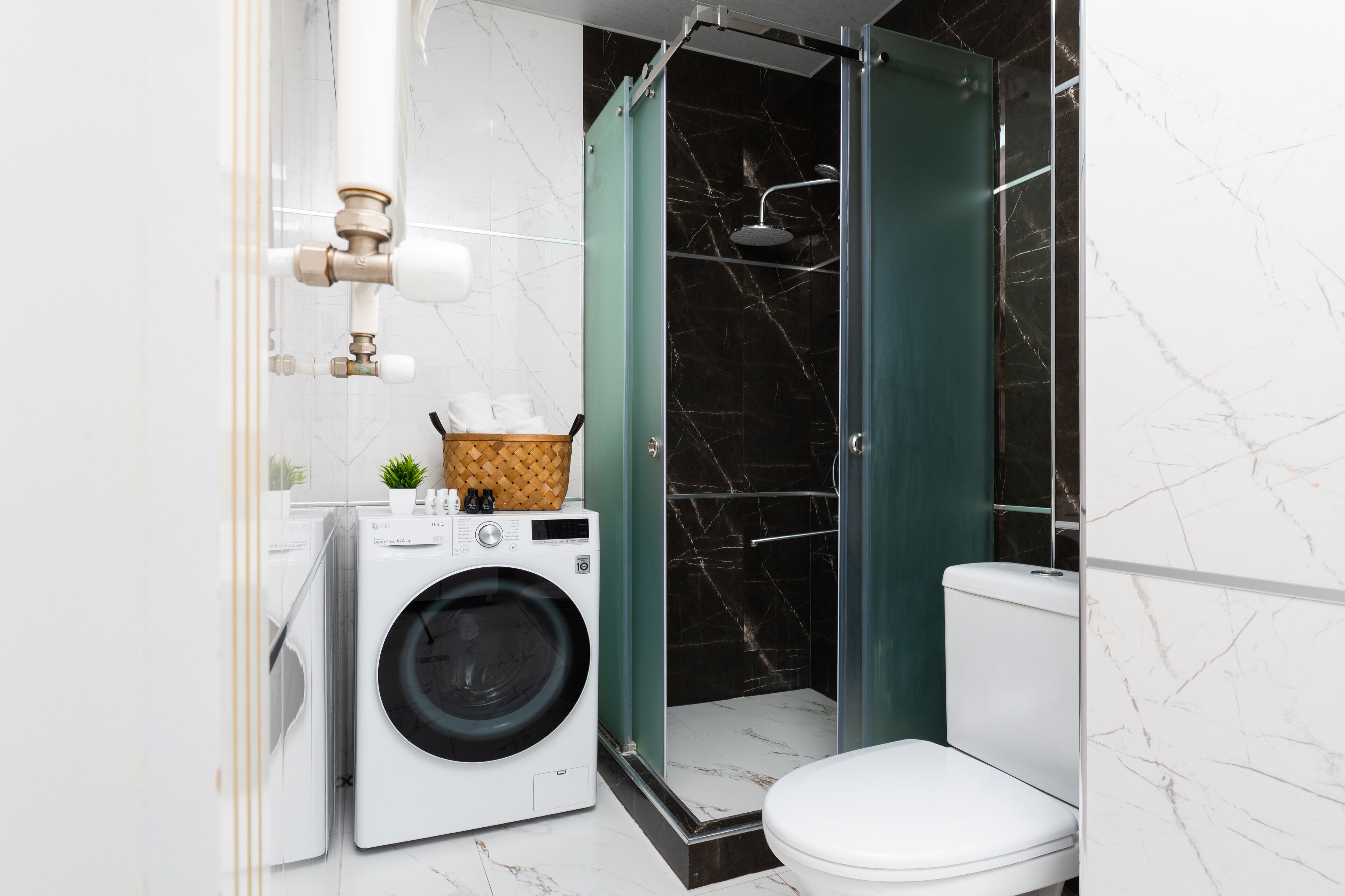 Une petite salle de bain équipée d’un lave-linge, de toilettes et d’une douche séparée par une paroi en verre.