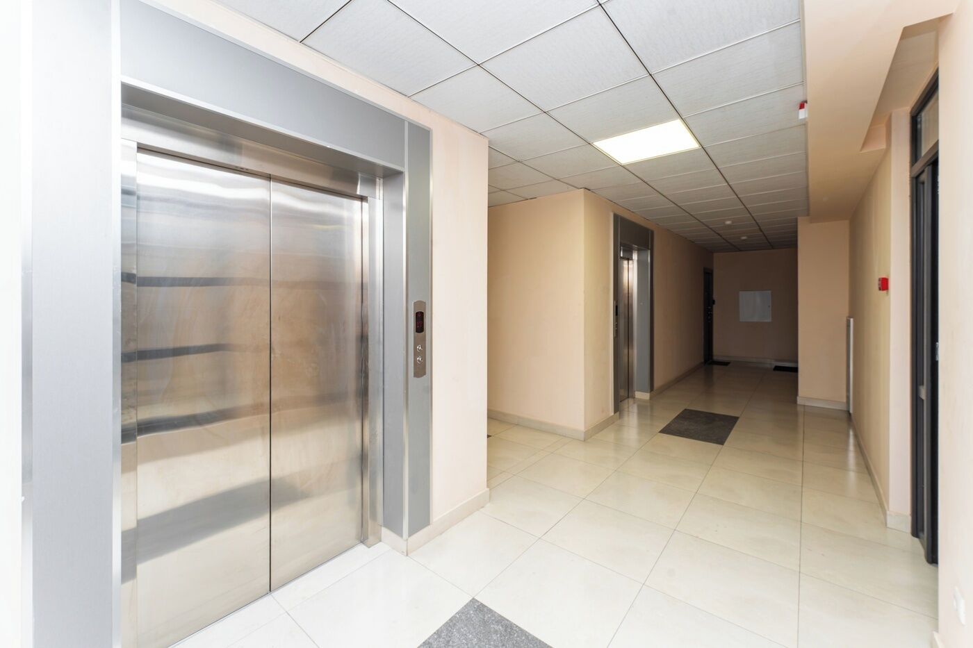 A hallway with two elevators and a tiled floor.