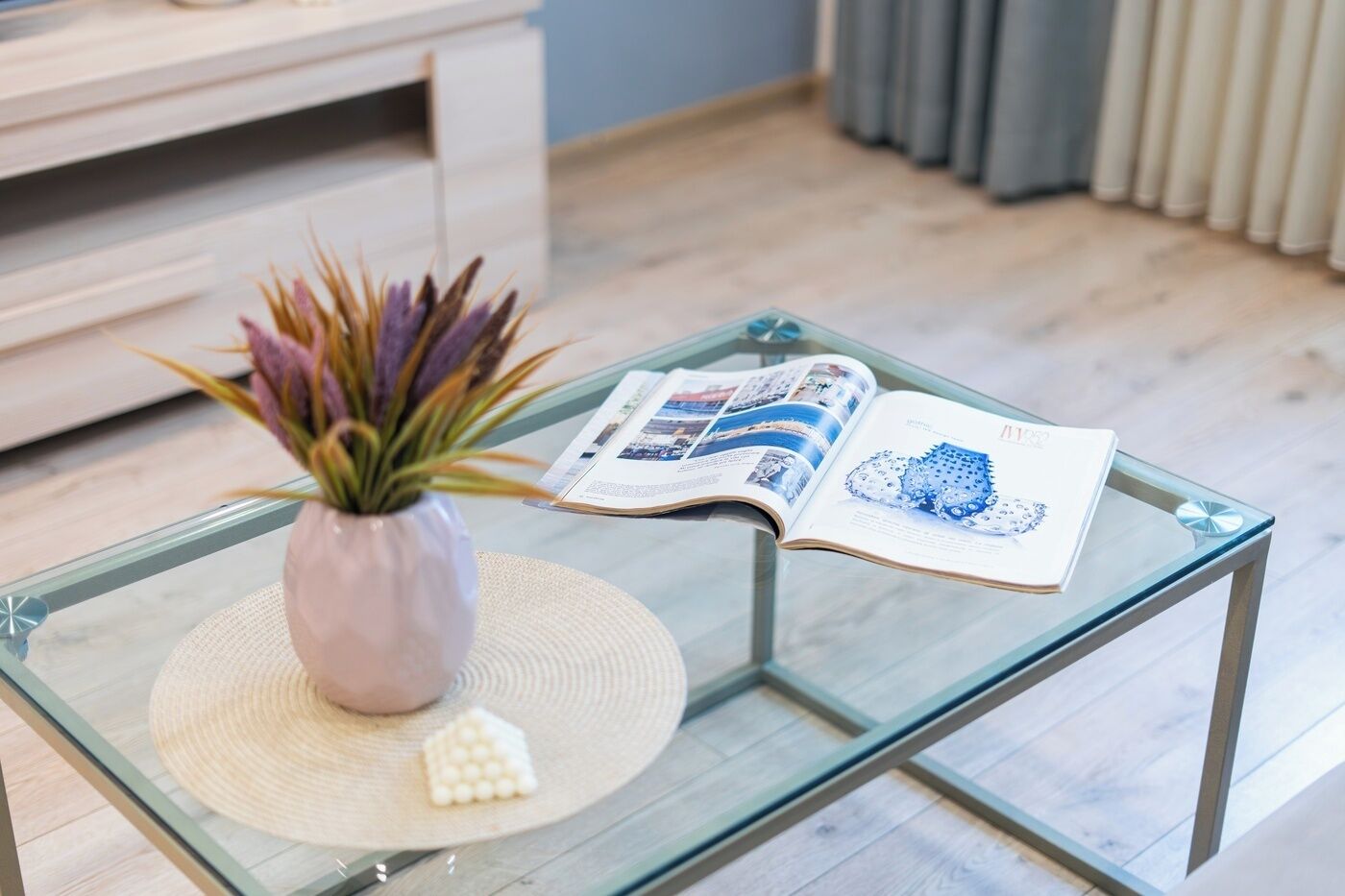 A glass coffee table with a magazine and a plant.