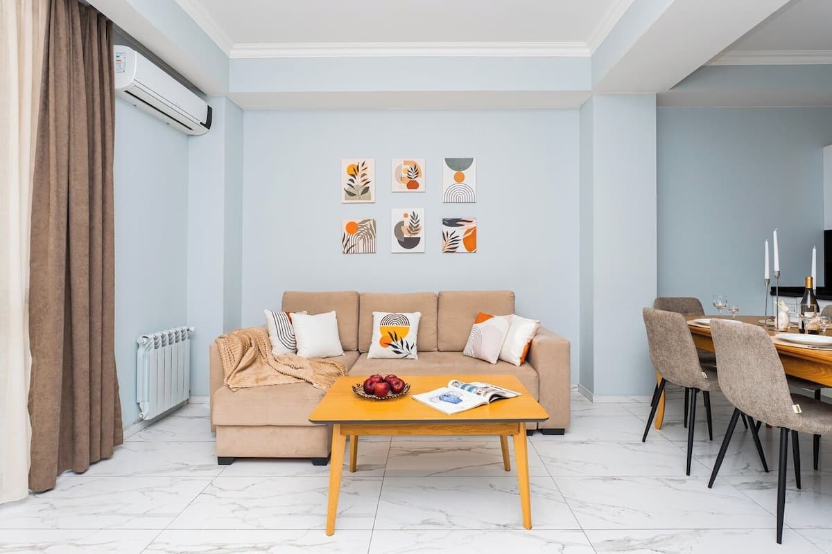 A modern living room with a beige sofa, a wooden coffee table, and a dining area with chairs and a table set for two.