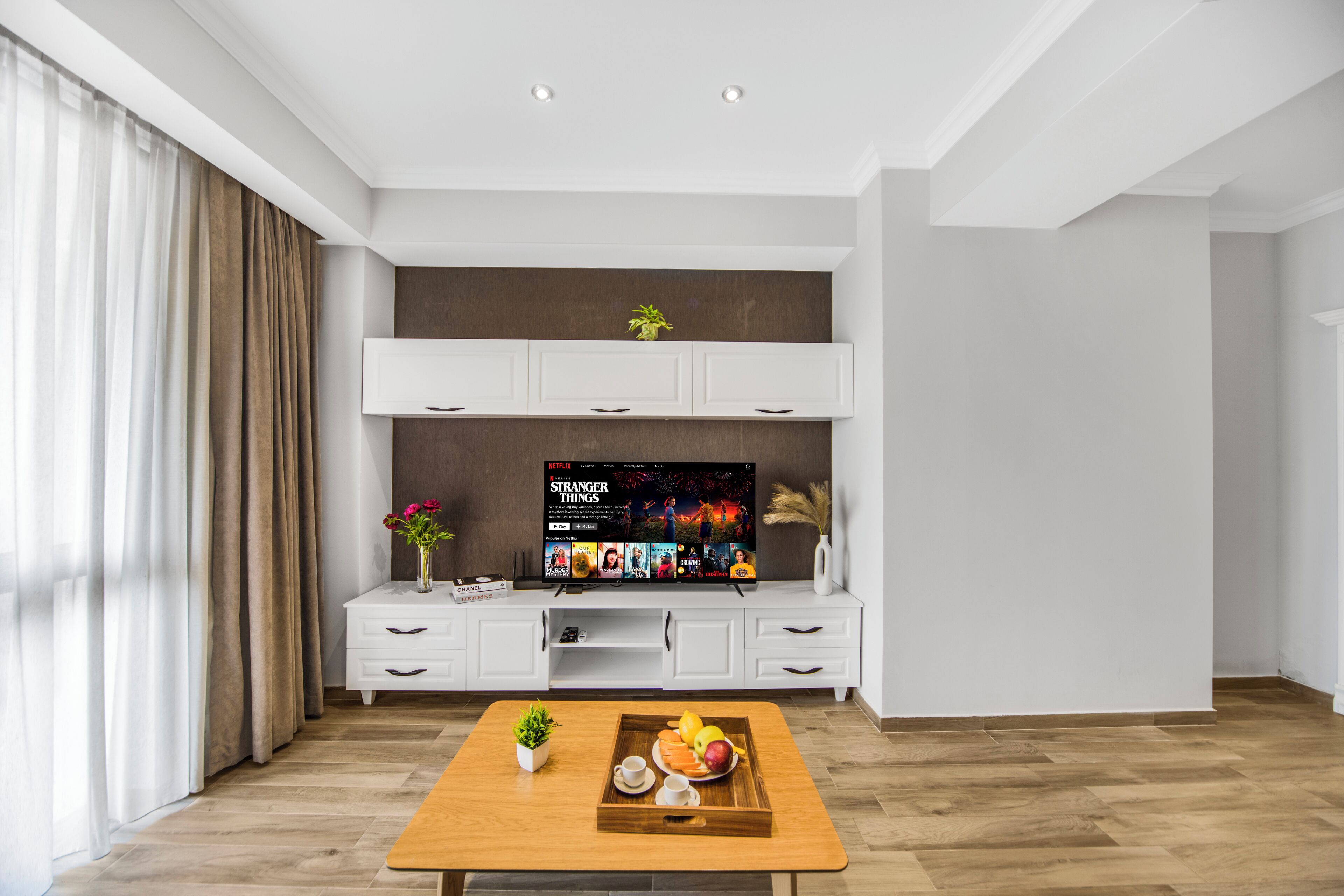 Un salon moderne avec une table basse en bois, un meuble de rangement blanc pour l’équipement audiovisuel et un téléviseur à écran plat affichant l’interface Netflix.