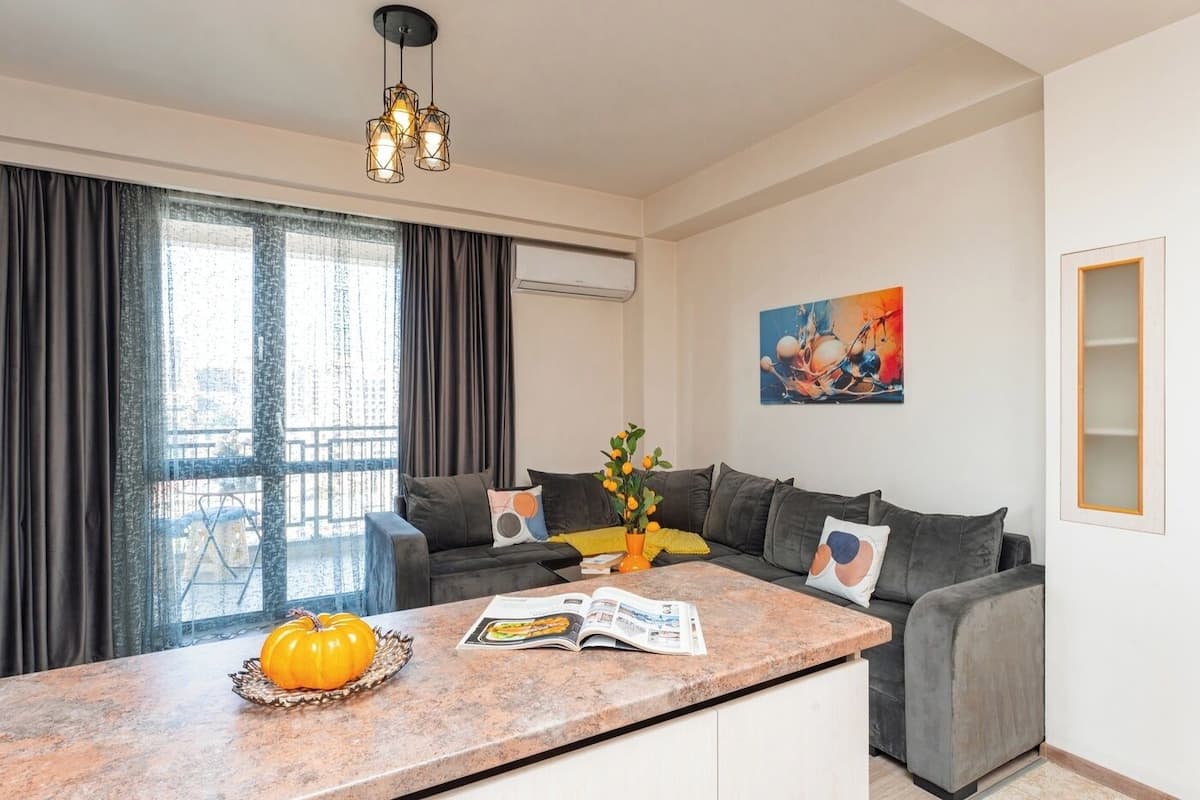 A modern living room with a grey sofa, a coffee table with a pumpkin, and a painting on the wall.