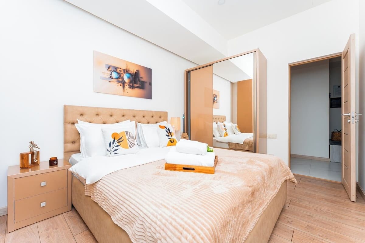 A modern bedroom with a large bed, a nightstand, a mirror, and a painting on the wall.
