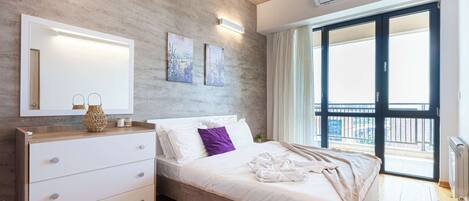 Un dormitorio moderno con suelo de madera, una cama grande con ropa de cama blanca, un aparador blanco, un espejo y dos luces fijadas a la pared.