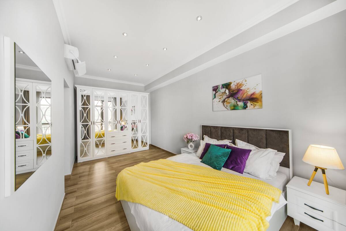A bedroom with a bed, bedside table, lamp, and a white wardrobe with a mirror.
