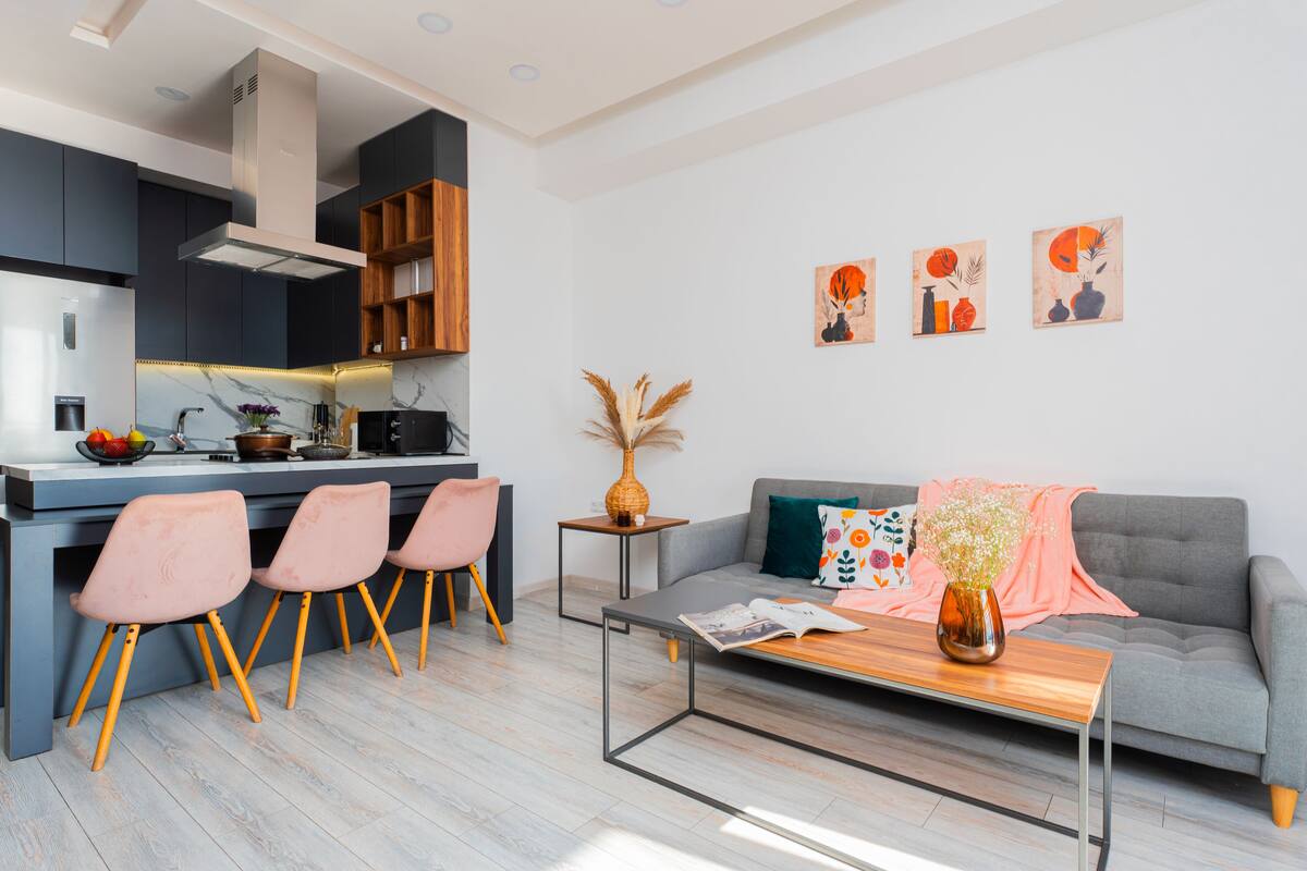 A modern kitchen with dark cabinets, a central island, and a dining area with pink chairs.