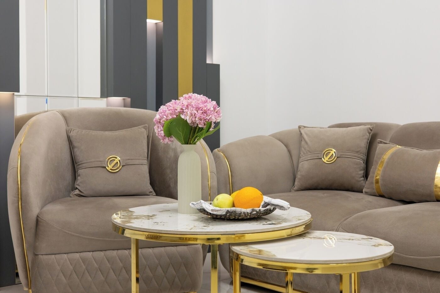 A modern living room with a sectional sofa, a small round table with a vase of flowers, and a fruit bowl.