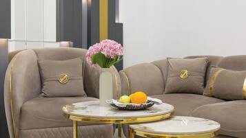 A modern living room with a sectional sofa, a small round table with a vase of flowers, and a fruit bowl.