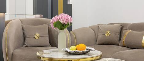 Uma sala de estar moderna com um sofá seccional, uma pequena mesa redonda com um vaso de flores e uma fruteira.