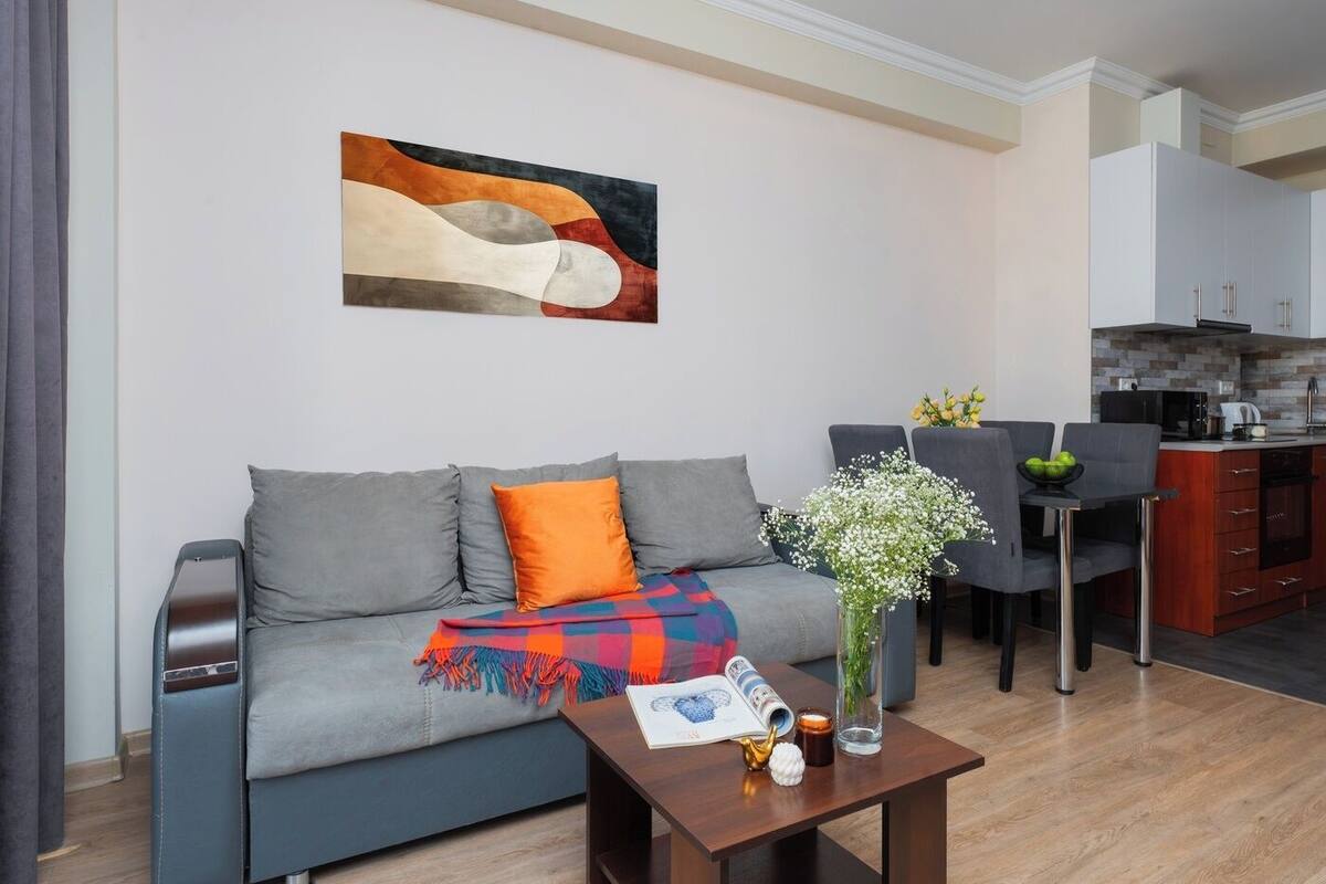 A modern living room with a grey sofa, a colorful throw blanket, and a coffee table with a magazine, a cup, and a vase with flowers.
