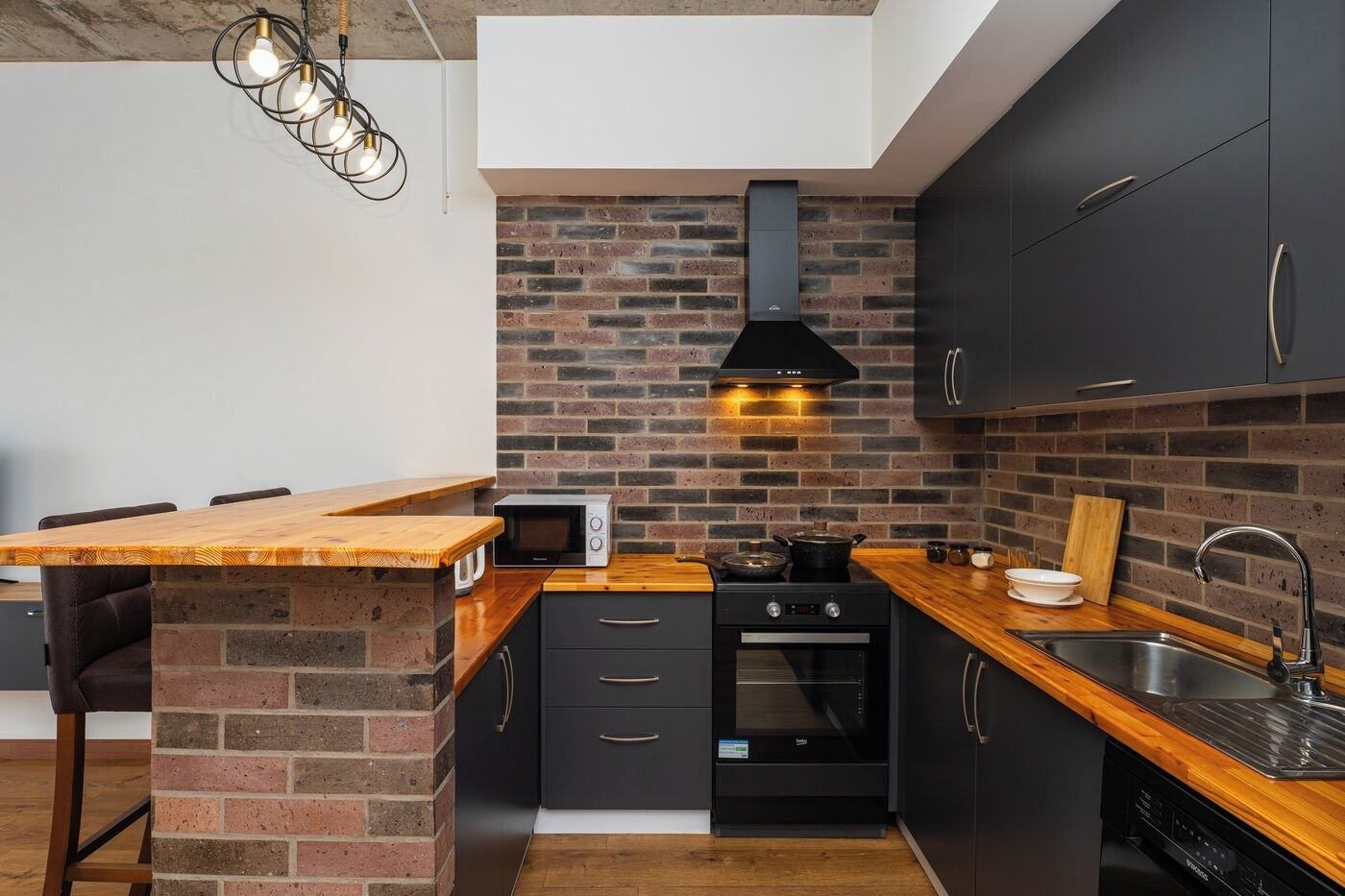 Una cocina compacta con salpicadero de ladrillo, una isla de madera y electrodomésticos modernos.