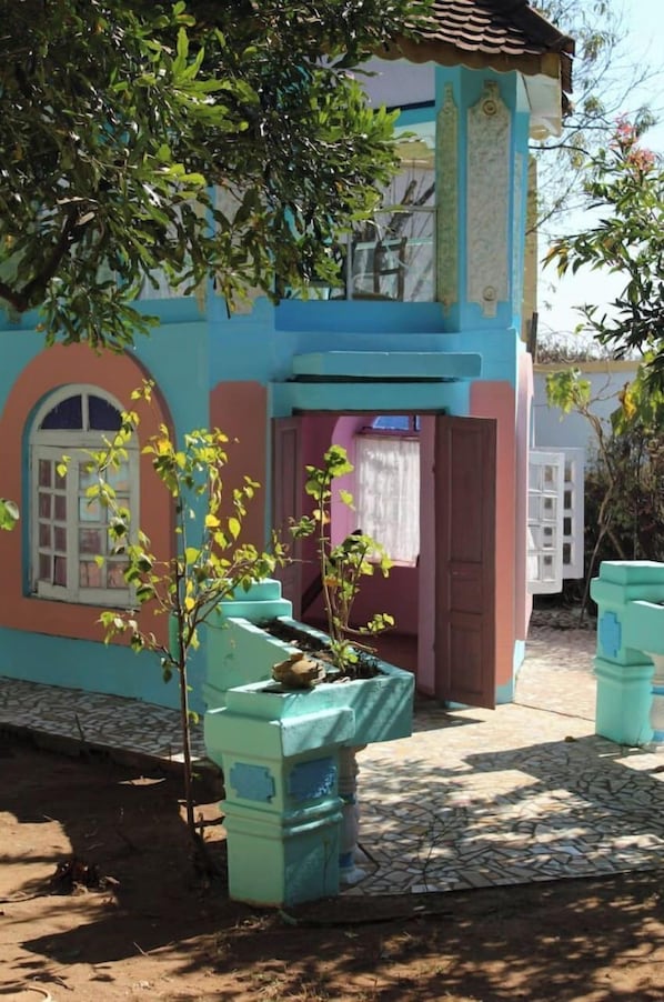 Un edificio colorido con entrada de baldosas y un pequeño árbol en una jardinera.