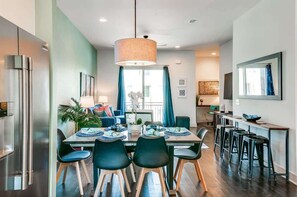 A modern kitchen with a dining area, featuring a large window, a hanging light fixture, and a bar counter with stools. - Nashville rooftop deck & game room house, sleeps 10 near broadway (Nashville)