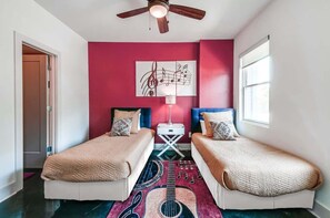 A room with two beds, a ceiling fan, a wall art piece, and a window.