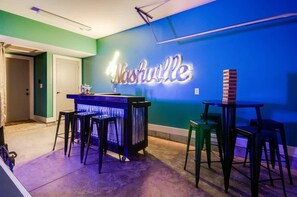 A bar area with a neon sign reading "Nashville" on a blue wall, a counter, stools, and a stack of bricks.