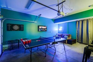A room with a ping pong table, dartboards, and a TV screen.