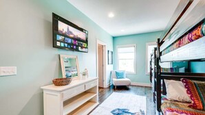 A room with a bed, a TV mounted on the wall, a white console table, and a window. - Music-themed Nashville home with game room, bar & bunk rooms, sleeps 10 (Nashville)