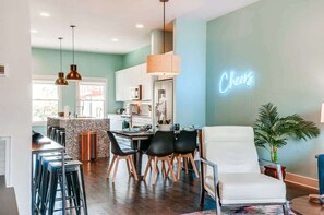 Une cuisine moderne avec un néon, un coin repas avec des chaises et un bar avec des tabourets.
