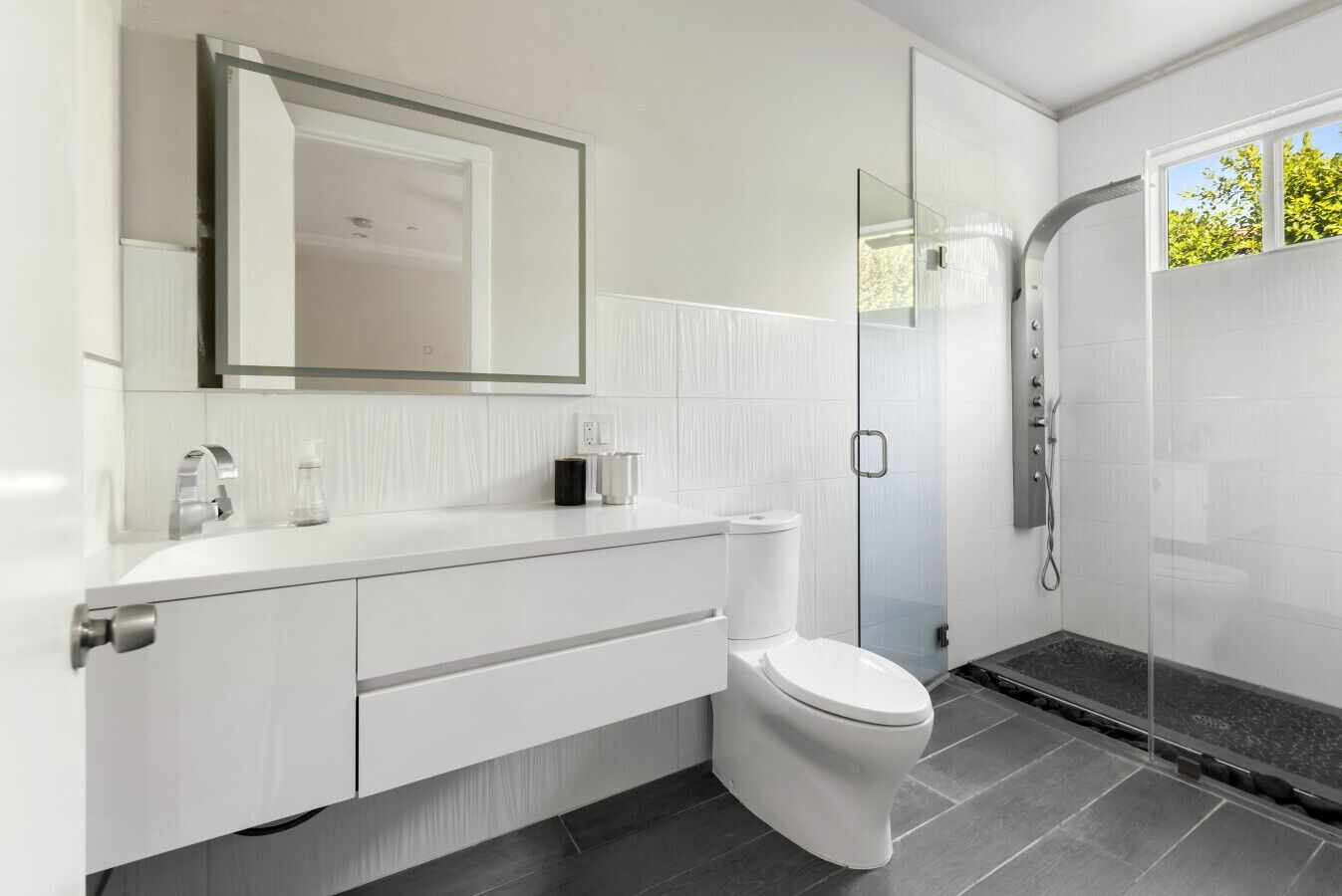 A modern bathroom with a white vanity, a toilet, a glass shower enclosure, and a large mirror above the vanity.