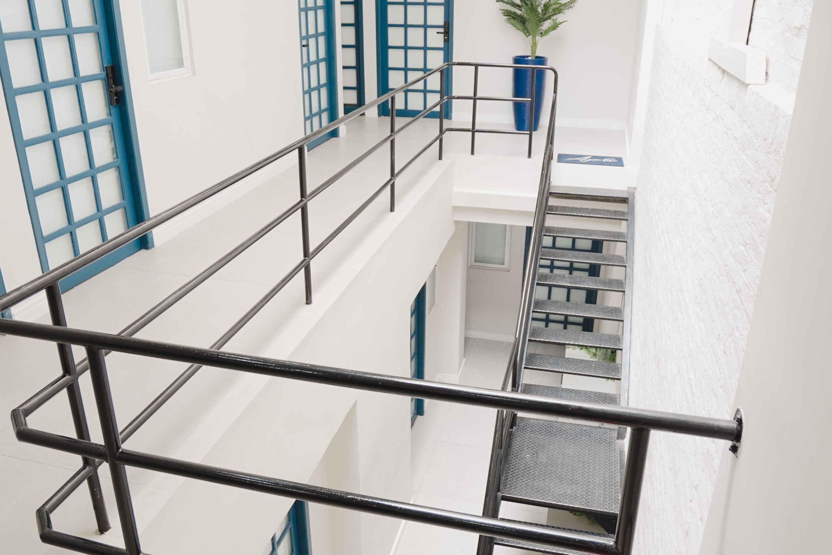 A multi-level interior with a metal railing, white walls, and blue accents on doors and railings.