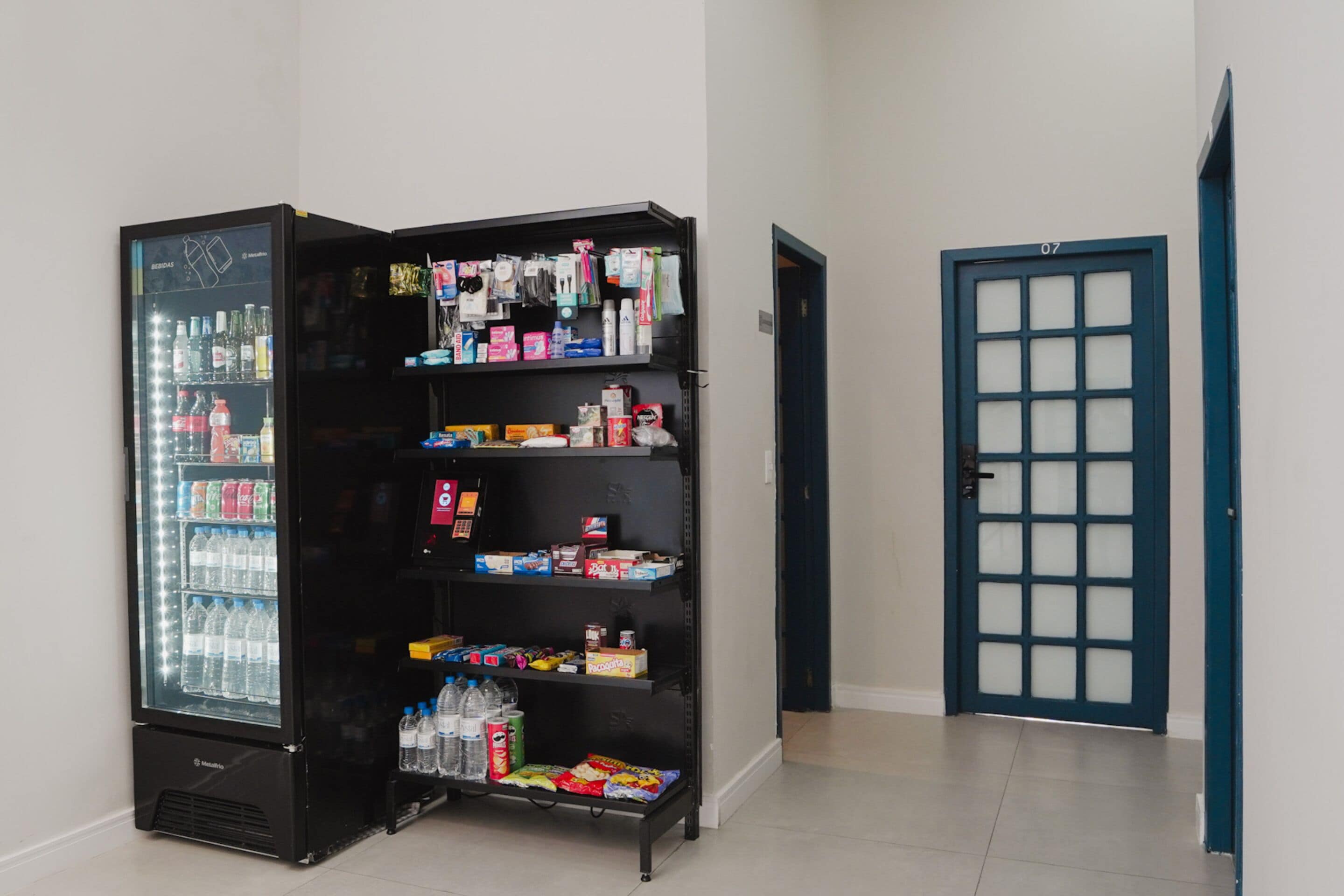 A vending machine stocked with beverages and snacks, a door with a number, and a tiled floor.