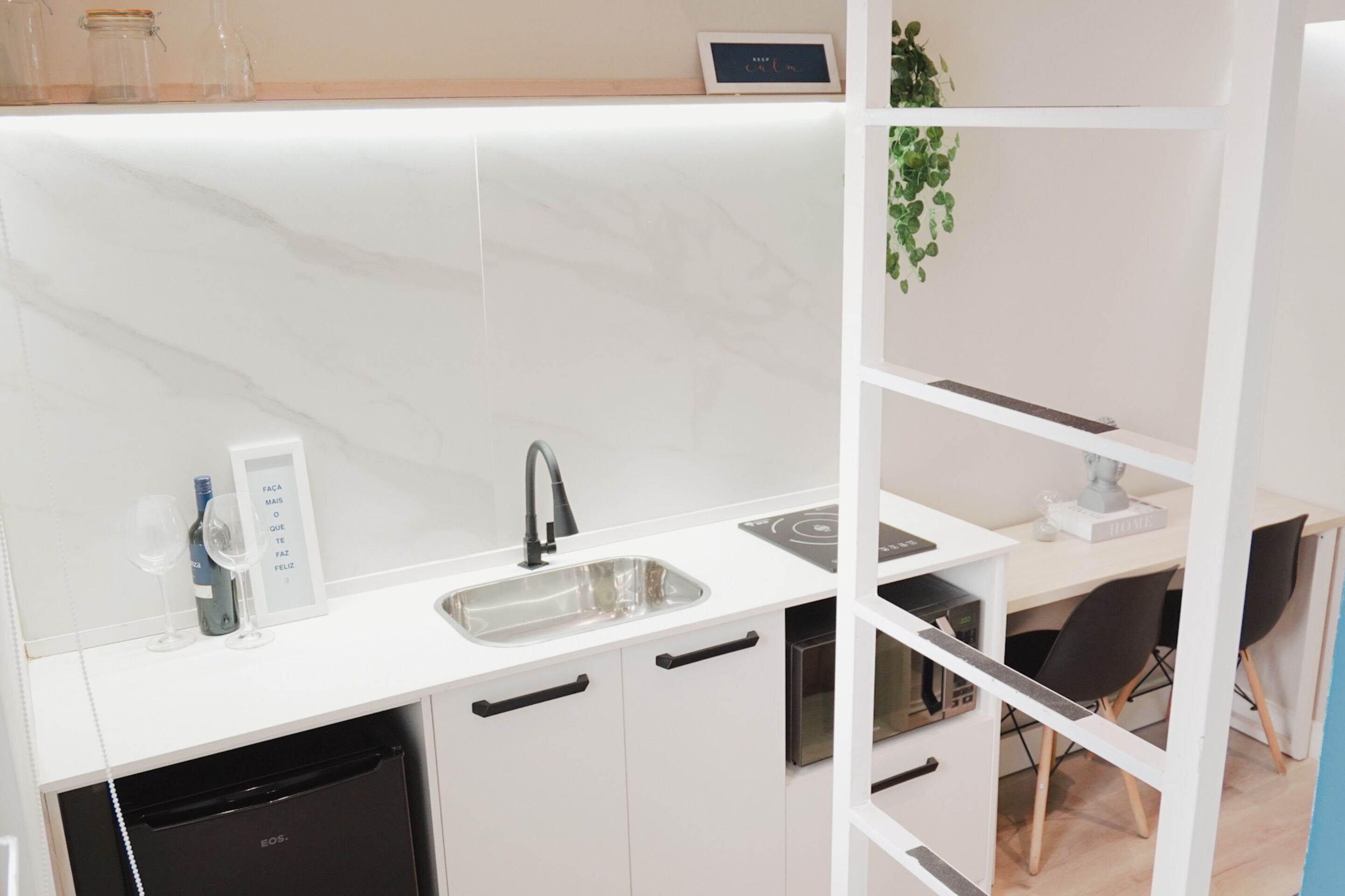 A modern kitchen with white cabinetry, a built-in dishwasher, a sink, and a countertop with wine glasses and a bottle.