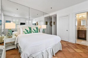 A hotel room with a large bed, two bedside tables with lamps, a mirror, and a door leading to a bathroom.
