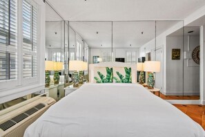 A hotel room with a large bed, two bedside lamps, a mirror, and a view of the outside through the window. - SpecialOfferPool/StepsToBeach/CharmStudio (Palm Beach)