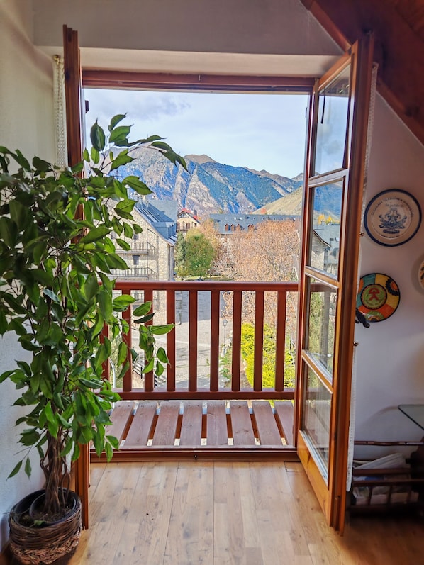 A balcony with a wooden floor, a potted plant, and a view of mountains.