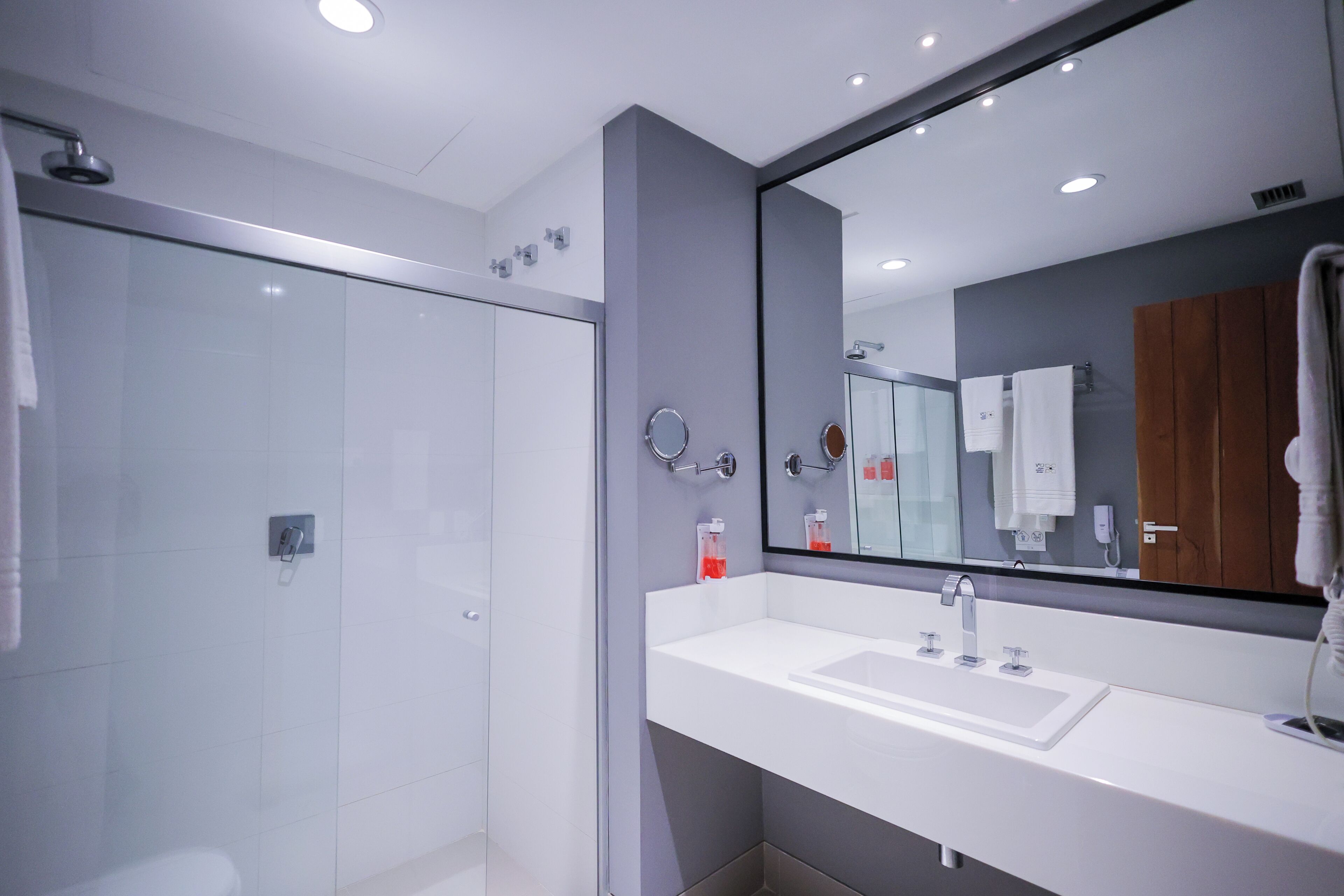 A modern bathroom with a glass shower enclosure, a white sink, and a large mirror.