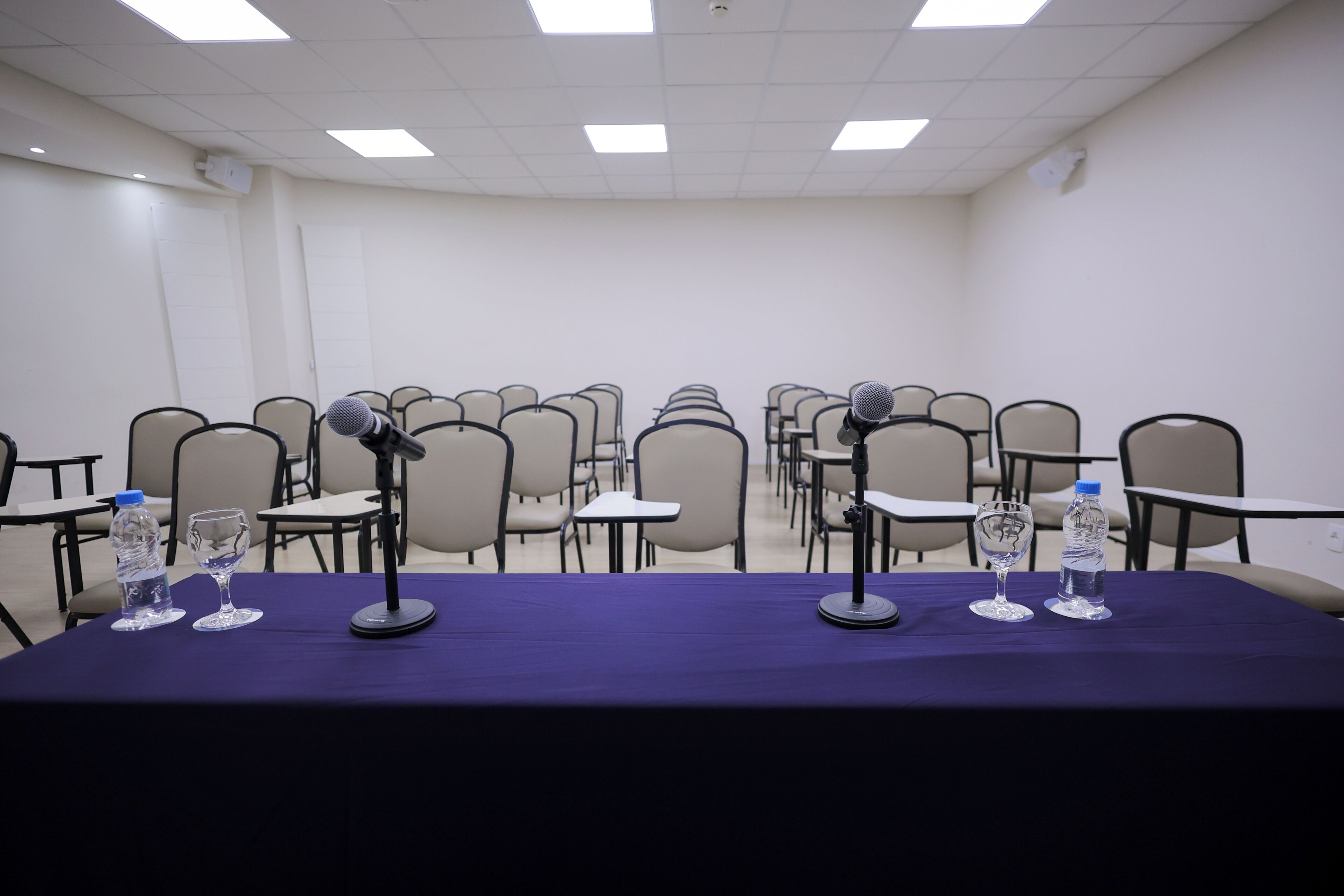 A conference room with a long table, multiple chairs, microphones, and water bottles.