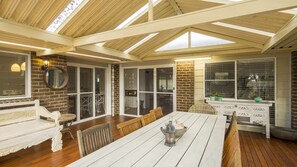Relax in this sunroom with a high ceiling, skylights, and a wooden deck perfect for casual dining.