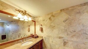 Un bany amb paret de marbre, un lavabo i un mirall amb il·luminació.