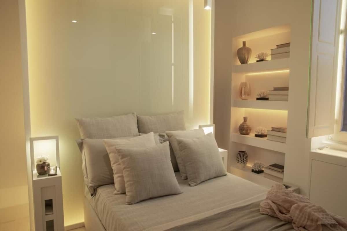 A modern bedroom with a bed, bedside tables, and a built-in shelving unit with decorative items.
