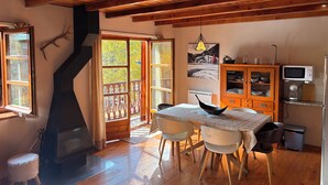 A cozy kitchen with wooden beams, a fireplace, a dining table with chairs, and a kitchen cabinet.