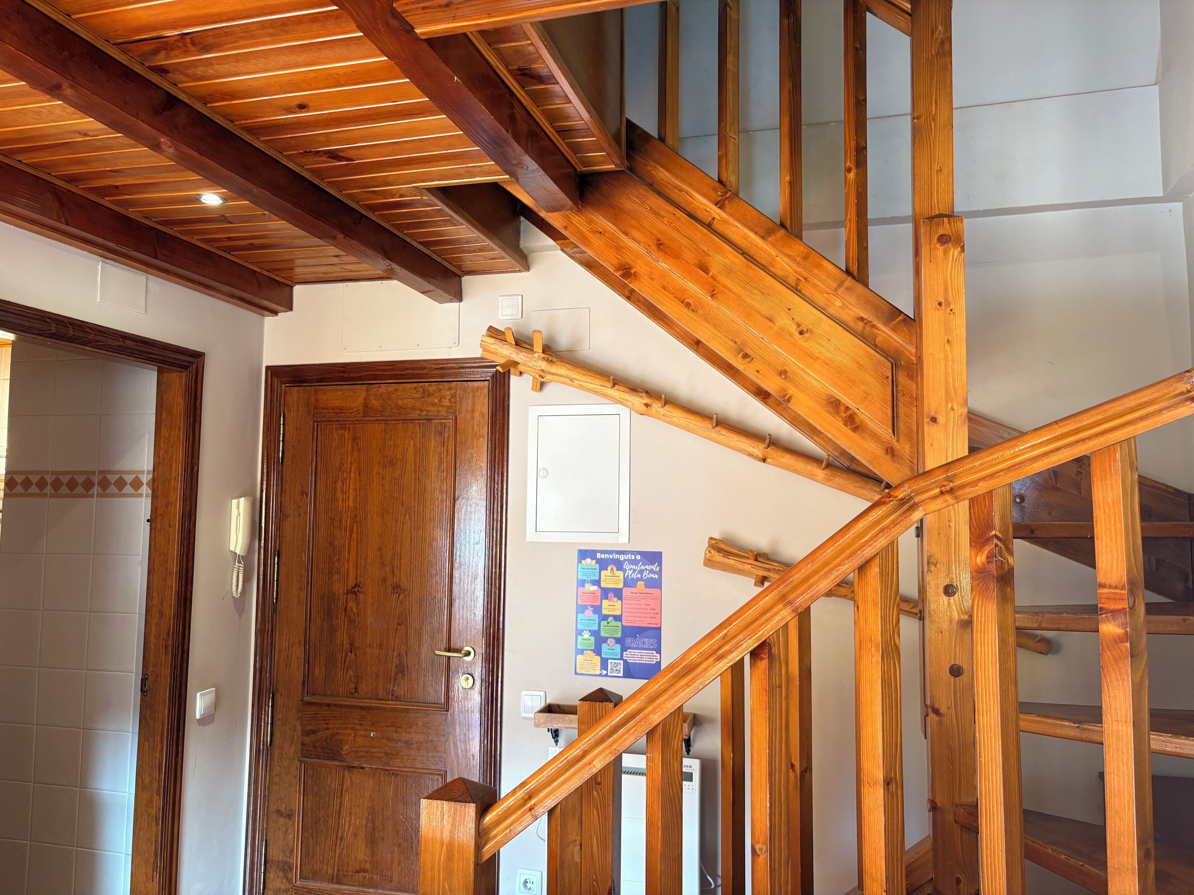 Un escalier en bois avec une rampe, une porte en bois et un interrupteur fixé au mur.