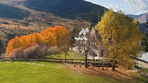 A grassy field with a stone building, a wooden fence, and trees with autumn foliage.