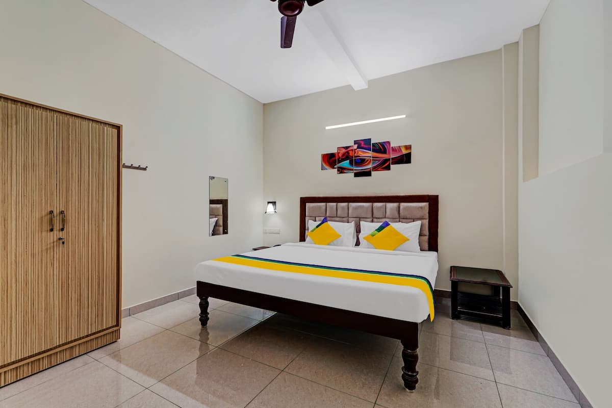 A bedroom with a bed, a wardrobe, a ceiling fan, a wall-mounted light, and a painting.