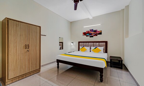 A bedroom with a bed, a wardrobe, a ceiling fan, a wall-mounted light, and a painting. - Itsy Hotels Green Villaa, 2 Km From Pondicherry Railway Station (Puducherry)