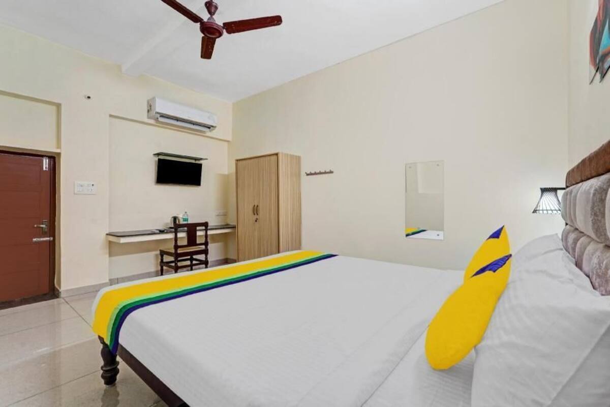 A hotel room with a bed, a desk, a wardrobe, a ceiling fan, and an air conditioning unit.