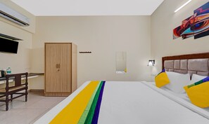 A hotel room with a bed, a wooden wardrobe, a desk with a chair, a flat-screen TV, and a colorful painting on the wall. - Itsy Hotels Green Villaa, 2 Km From Pondicherry Railway Station (Puducherry)