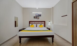 A hotel room with a large bed, a nightstand, a mirror, and a wall-mounted light fixture. - Itsy Hotels Green Villaa, 2 Km From Pondicherry Railway Station (Puducherry)