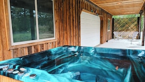 Un jacuzzi con cubierta de madera, un ventanal grande y un porche cubierto con sillas.