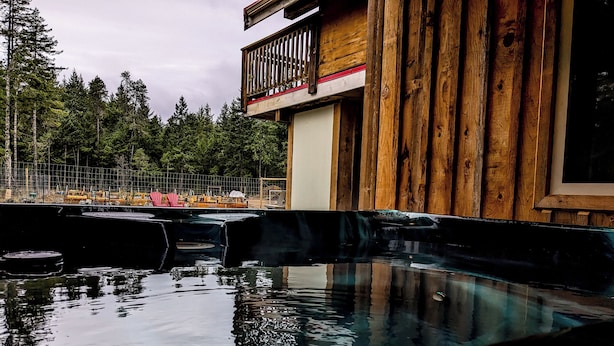 Una cabaña de madera con balcón de madera que da a una piscina cristalina.