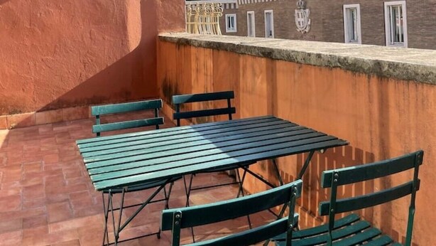 A rooftop terrace with a table and chairs, a brick wall, and a view of a historical building with a dome. - Incantevole Attico in Via Del Corso (Roma)