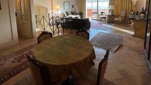 A spacious living area with a round table and chairs, a piano, and a dining area with a table and chairs. - Incantevole Attico in Via Del Corso (Roma)