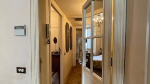A hallway with a tiled floor, a door leading to a bathroom, and a window with a view of a bedroom. - Incantevole Attico in Via Del Corso (Roma)